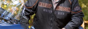 Man standing behind harley davidson wearing dew rag, leather jacket & sunglasses