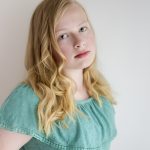young girl wearing green top posing for headshot on white wall