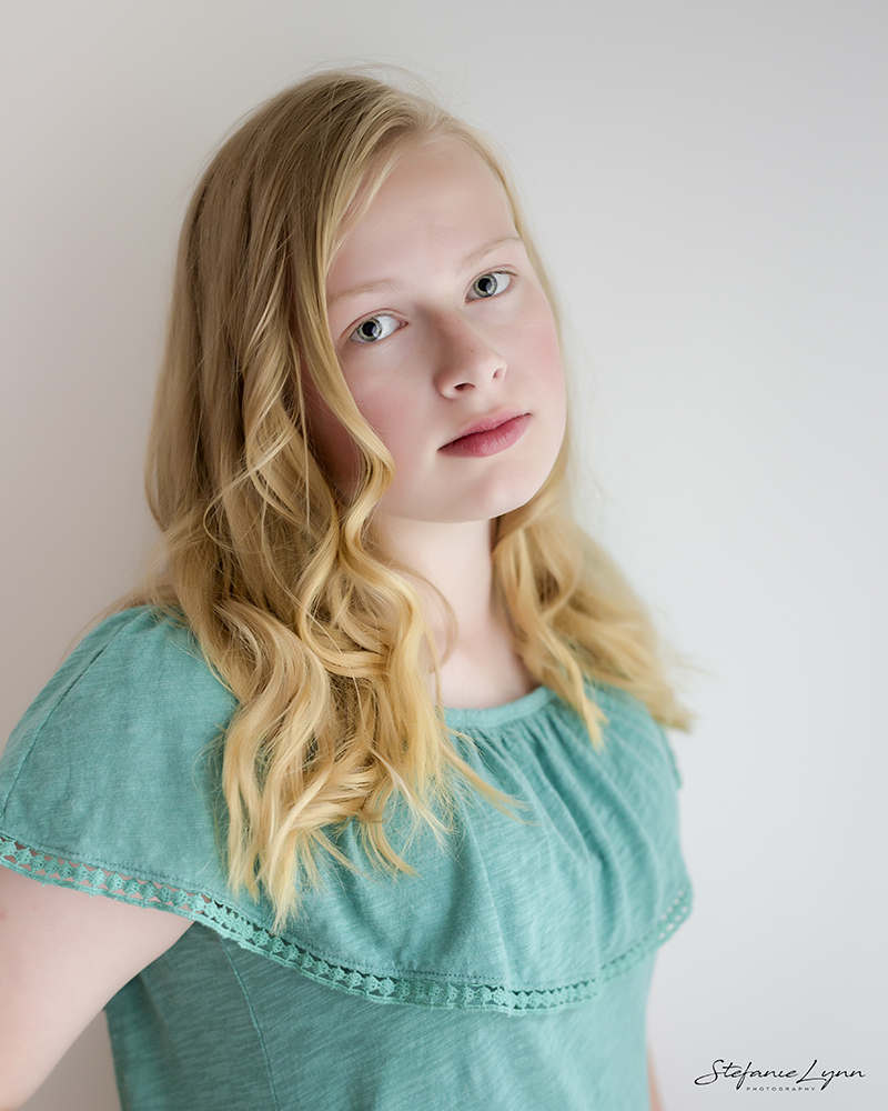young girl wearing green top posing for headshot on white wall