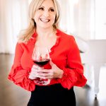 Woman standing with a glass of red wine, smiling & looking off