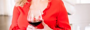 Woman standing with a glass of red wine, smiling & looking off