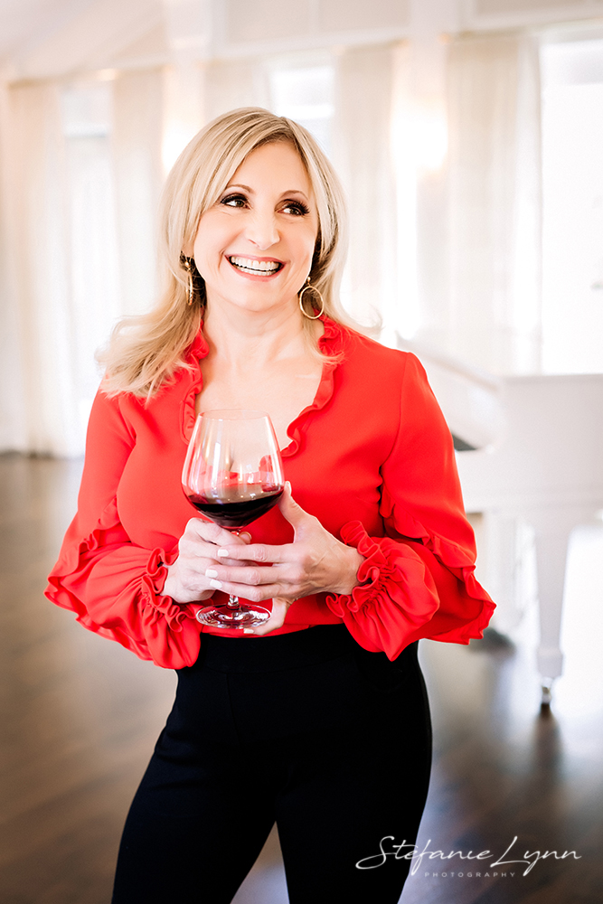 Woman standing with a glass of red wine, smiling & looking off 